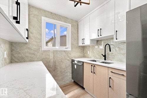 White high-gloss upper cabinetry, natural wood-finish lower cabinetry, light-toned stone-finish backsplash, white stone-finish countertops, and stainless steel appliances - 18307 66 Avenue Nw, Edmonton, AB - Indoor Photo Showing Kitchen With Double Sink