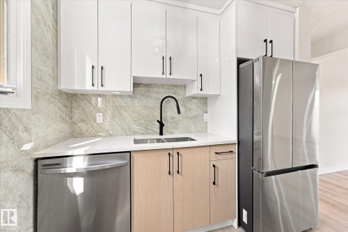 Sleek kitchen featuring white upper cabinetry, light wood-finish lower cabinetry, a stainless steel refrigerator, and a stainless steel dishwasher - 18307 66 Avenue Nw, Edmonton, AB - Indoor Photo Showing Kitchen With Double Sink With Upgraded Kitchen