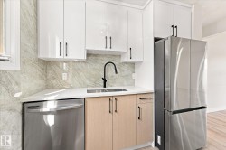 Sleek kitchen featuring white upper cabinetry, light wood-finish lower cabinetry, a stainless steel refrigerator, and a stainless steel dishwasher - 