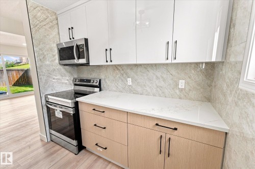 White upper cabinetry with black hardware, wood-finish lower cabinetry, stone-finish countertop, stainless steel range, and matching stainless steel microwave - 18307 66 Avenue Nw, Edmonton, AB - Indoor Photo Showing Kitchen