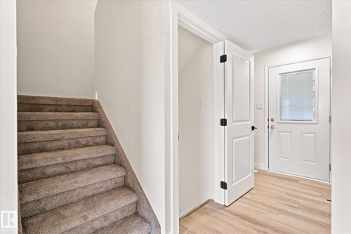 Carpeted staircase, light wood-finish flooring, white paneled door with matte black hardware, white exterior door with rectangular glass insert, and recessed lighting - 18307 66 Avenue Nw, Edmonton, AB - Indoor Photo Showing Other Room