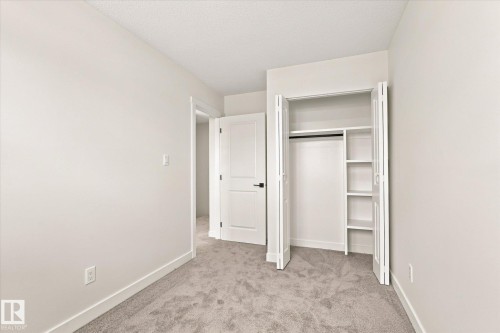 White interior walls, light-toned carpeting, white bi-fold closet doors, built-in closet shelving, and a white interior door with dark hardware - 18307 66 Avenue Nw, Edmonton, AB - Indoor Photo Showing Other Room