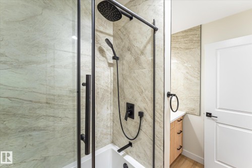Bathtub and shower combination with full-height tile surround, matte black fixtures, and glass enclosure - 18307 66 Avenue Nw, Edmonton, AB - Indoor Photo Showing Bathroom
