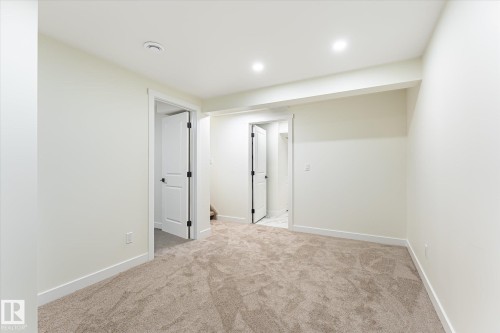 Neutral tone wall paint, recessed lighting, carpet flooring, two-panel interior doors with dark hardware, and white trim - 18307 66 Avenue Nw, Edmonton, AB - Indoor Photo Showing Other Room