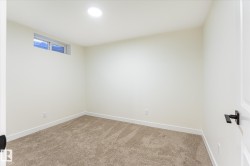 Recessed ceiling lighting, a single horizontal window, clean white walls, light brown carpet, and a white paneled door with a matte black handle - 
