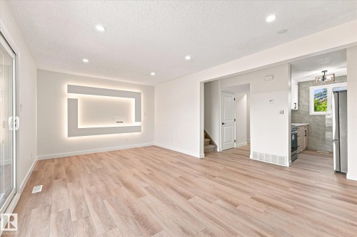 Recessed lighting, wood-finish flooring, built-in wall feature with backlighting, sliding glass door, and a partial kitchen with stainless steel appliances - 18307 66 Avenue Nw, Edmonton, AB - Indoor Photo Showing Other Room