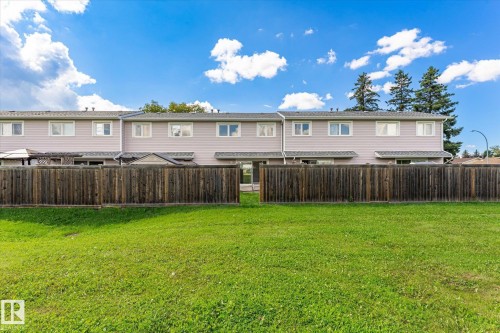 Expansive backyard featuring a manicured lawn and sturdy wood-finish privacy fencing, with mature evergreen trees providing natural screening and backdrop - 18307 66 Avenue Nw, Edmonton, AB - Outdoor