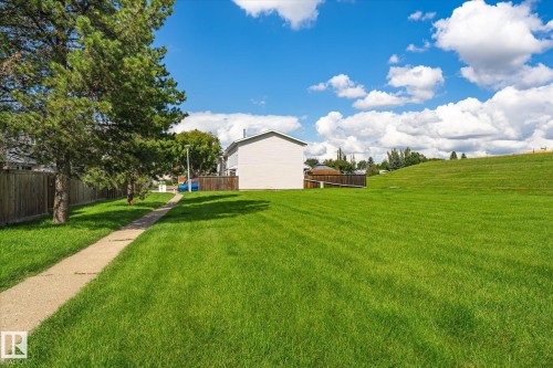 Expansive green space featuring a concrete pathway, mature trees, and a sloped grassy area - 18307 66 Avenue Nw, Edmonton, AB - Outdoor