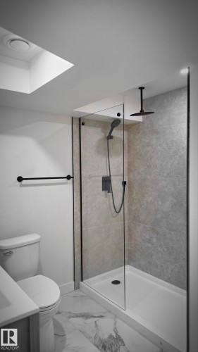 Walk-in shower with a glass enclosure, black-finish fixtures, and a ceiling-mounted rainfall shower head - 18307 66 Avenue Nw, Edmonton, AB - Indoor Photo Showing Bathroom