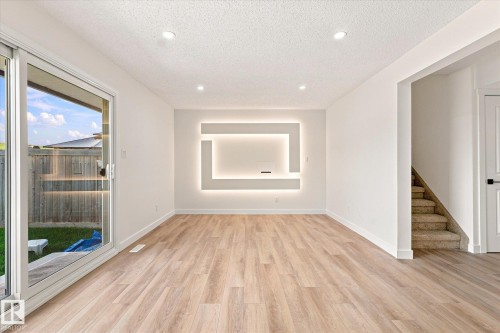 Recessed ceiling lighting, wood-finish flooring, sliding glass door, built-in wall feature with backlighting, and carpeted stairs - 18307 66 Avenue Nw, Edmonton, AB - Indoor Photo Showing Other Room