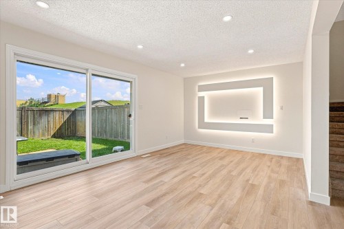 Light wood-finish flooring, recessed ceiling lighting, a decorative wall panel with integrated backlighting, and sliding glass doors opening to a fenced backyard - 18307 66 Avenue Nw, Edmonton, AB - Indoor