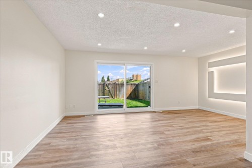 Wood-finish flooring throughout, recessed ceiling lighting, sliding glass door, and integrated wall lighting feature - 18307 66 Avenue Nw, Edmonton, AB - Indoor Photo Showing Other Room
