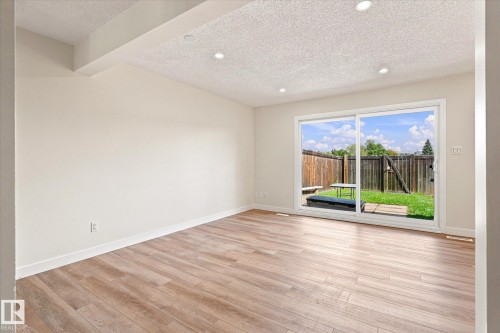 Wood-finish flooring with white baseboards, recessed ceiling lighting, and a sliding glass door - 18307 66 Avenue Nw, Edmonton, AB - Indoor Photo Showing Other Room