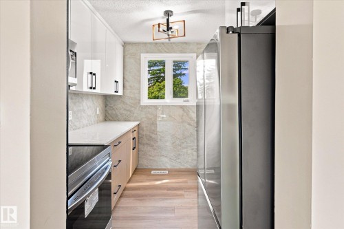 Kitchen featuring light wood-finish flooring, white upper cabinetry, light wood-finish lower cabinetry, and a window - 18307 66 Avenue Nw, Edmonton, AB - Indoor Photo Showing Kitchen