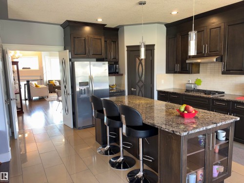 Kitchen featuring dark wood-finish cabinetry, stainless steel appliances, a multi-tone island with a granite-style countertop, and recessed lighting - 1452 36A Avenue Nw, Edmonton, AB - Indoor Photo Showing Kitchen With Upgraded Kitchen