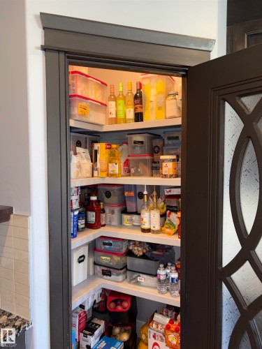 Walk-in pantry featuring built-in shelving, decorative door, and a tiled wall - 1452 36A Avenue Nw, Edmonton, AB - Indoor Photo Showing Other Room