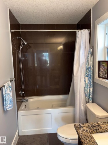 Built-in tub with dark tile surround and a shower fixture - 1452 36A Avenue Nw, Edmonton, AB - Indoor Photo Showing Bathroom