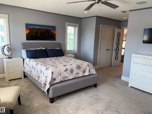 Spacious primary bedroom suite with gray upholstered bed frame, neutral wall finishes, ceiling fan with integrated lighting, dual white dresser units with ample storage, and direct access to an ensuite bathroom - 1452 36A Avenue Nw, Edmonton, AB - Indoor Photo Showing Bedroom