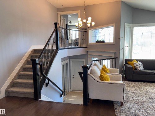 Staircase with dark wood newel posts and wrought iron balusters, hardwood flooring, upper-level landing with matching railing, and large arched windows with white trim - 1452 36A Avenue Nw, Edmonton, AB - Indoor Photo Showing Other Room