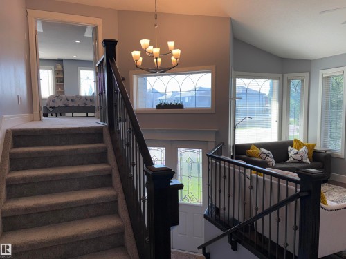 Carpeted staircase with wrought iron railing, vaulted ceilings, decorative transom windows, and a multi-paneled front door with decorative glass inserts - 1452 36A Avenue Nw, Edmonton, AB - Indoor Photo Showing Other Room