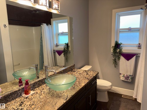 Vanity with a vessel sink, stone countertop, wood-finish cabinet, and chrome faucet - 1452 36A Avenue Nw, Edmonton, AB - Indoor Photo Showing Bathroom