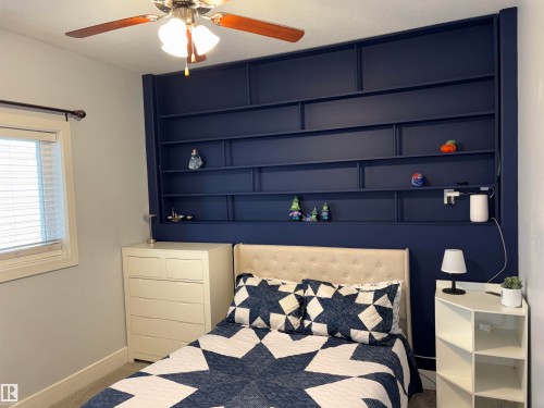 Built-in shelving unit with a dark-toned finish, ceiling fan with integrated lighting, window with blinds, and light gray wall paint - 1452 36A Avenue Nw, Edmonton, AB - Indoor Photo Showing Bedroom
