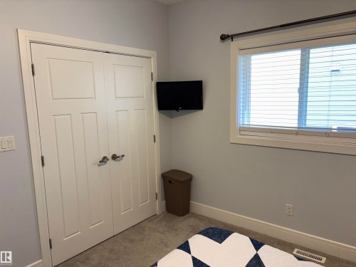 White paneled bi-fold doors, light gray wall paint, window with white trim, and light-colored carpet - 1452 36A Avenue Nw, Edmonton, AB - Indoor