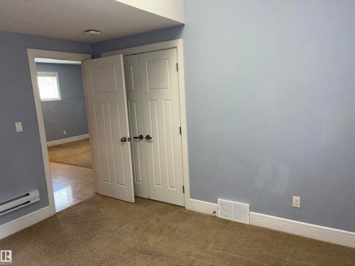 Neutral tone wall paint, bi-fold closet doors, wall-to-wall carpeting, white trim, and wall-mounted baseboard heater - 1452 36A Avenue Nw, Edmonton, AB - Indoor Photo Showing Other Room