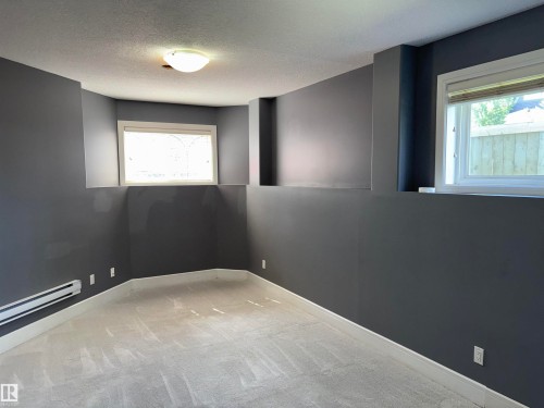 Neutral-toned carpet flooring, multiple windows providing natural light, and a flush-mount ceiling light fixture - 1452 36A Avenue Nw, Edmonton, AB - Indoor