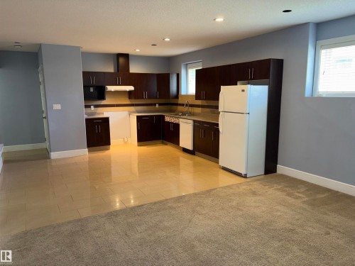 Open-concept kitchen with dark wood-finish cabinetry, light-toned countertops, and a tile backsplash - 1452 36A Avenue Nw, Edmonton, AB - Indoor Photo Showing Kitchen
