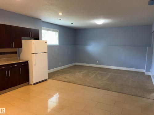 Dark wood-finish cabinetry with a light countertop, white refrigerator, and tile flooring - 1452 36A Avenue Nw, Edmonton, AB - Indoor Photo Showing Kitchen