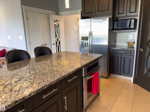Kitchen island with a natural stone countertop, stainless steel oven, and dark wood-finish cabinetry - 1452 36A Avenue Nw, Edmonton, AB - Indoor Photo Showing Kitchen