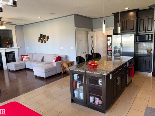 Open-concept living space featuring a substantial kitchen island with a granite countertop, stainless steel appliances, and dark wood-finish cabinetry - 1452 36A Avenue Nw, Edmonton, AB - Indoor Photo Showing Kitchen With Upgraded Kitchen