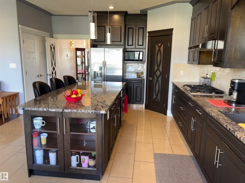 Expansive kitchen featuring a large island with built-in glass-front cabinetry, granite countertops, and dark wood-finish cabinetry - 1452 36A Avenue Nw, Edmonton, AB - Indoor Photo Showing Kitchen With Upgraded Kitchen