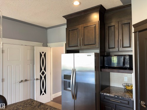 Stainless steel refrigerator, integrated microwave, dark wood-finish cabinetry, granite countertop, and decorative pantry door - 1452 36A Avenue Nw, Edmonton, AB - Indoor Photo Showing Kitchen