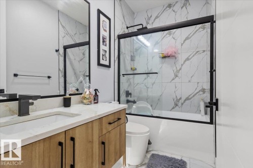 Modern bathroom featuring a wood-finish vanity with a built-in sink, solid surface countertop, and matte black fixtures - 6903 169 Avenue Nw, Edmonton, AB - Indoor Photo Showing Bathroom