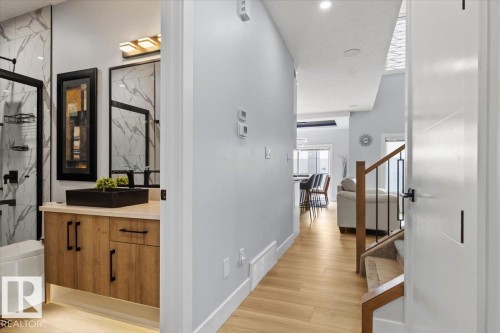 Wood-finish flooring, staircase with wood handrail and metal spindles, vanity with wood-look cabinetry and black vessel sink, and large framed mirror - 6903 169 Avenue Nw, Edmonton, AB - Indoor Photo Showing Other Room