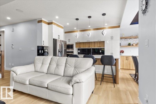 Contemporary kitchen featuring stainless steel appliances, white cabinetry with wood-finish accents, and a breakfast bar with seating - 6903 169 Avenue Nw, Edmonton, AB - Indoor Photo Showing Living Room
