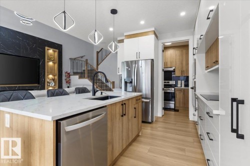 Kitchen island with a white countertop and integrated sink, stainless steel dishwasher, wood-finish cabinetry, and contemporary pendant lighting - 6903 169 Avenue Nw, Edmonton, AB - Indoor Photo Showing Kitchen With Upgraded Kitchen