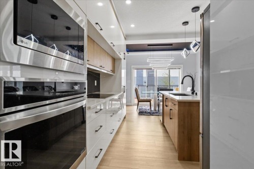 Integrated stainless steel appliances, wood-finish flooring, white cabinetry, wood-tone island with an undermount sink, and modern pendant lighting - 6903 169 Avenue Nw, Edmonton, AB - Indoor Photo Showing Kitchen With Upgraded Kitchen