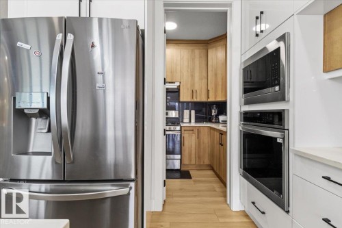 Stainless steel French door refrigerator, built-in microwave, and built-in oven complement the light wood-finish flooring and wood cabinetry - 6903 169 Avenue Nw, Edmonton, AB - Indoor Photo Showing Kitchen