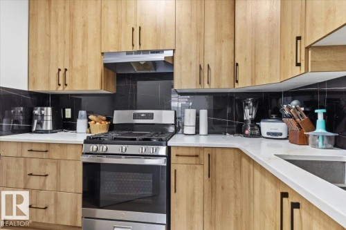 Wood-finish cabinetry, white countertops, black tile backsplash, stainless steel range, and stainless steel range hood - 6903 169 Avenue Nw, Edmonton, AB - Indoor Photo Showing Kitchen