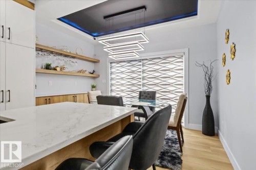 Quartz-finish island countertop, recessed ceiling with accent lighting, linear chandelier, light wood-finish flooring, and built-in shelving with integrated wine glass rack - 6903 169 Avenue Nw, Edmonton, AB - Indoor Photo Showing Other Room