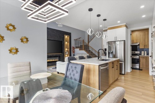Kitchen island with quartz countertop and undermount sink, stainless steel appliances, built-in electric fireplace, wood-finish flooring, and a modern stair railing - 6903 169 Avenue Nw, Edmonton, AB - Indoor Photo Showing Kitchen With Upgraded Kitchen