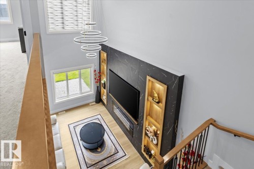 Two-story interior with a modern chandelier, light wood-finish flooring, and a built-in media wall featuring integrated shelving - 6903 169 Avenue Nw, Edmonton, AB - Indoor Photo Showing Other Room