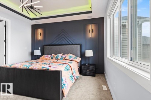Modern accent wall with integrated sconces, contemporary ceiling light fixture, recessed ceiling with ambient lighting, wall-to-wall carpeting, and a large multi-pane window - 6903 169 Avenue Nw, Edmonton, AB - Indoor Photo Showing Bedroom