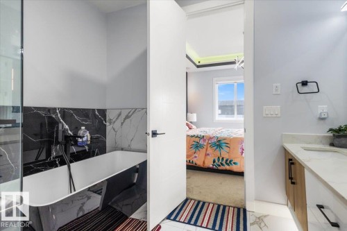 Freestanding soaking tub with black and white marble-look tile surround, dual-tone vanity with light wood and white cabinetry, quartz countertop, and a single undermount sink - 6903 169 Avenue Nw, Edmonton, AB - Indoor Photo Showing Bathroom