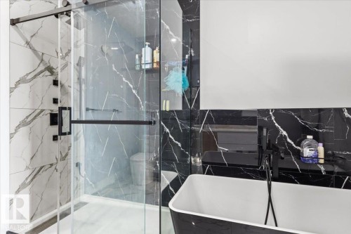 Shower enclosure with sliding glass door, black hardware, and large format white and black veined wall tile - 6903 169 Avenue Nw, Edmonton, AB - Indoor Photo Showing Bathroom
