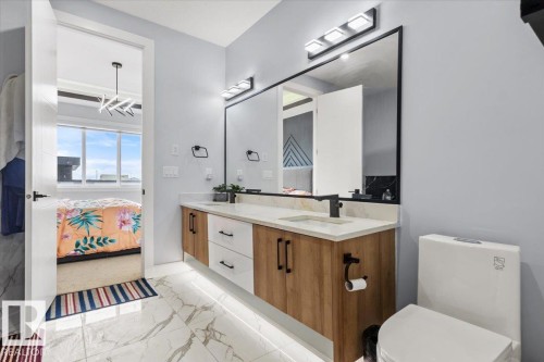 Modern primary bathroom featuring a wood-finish vanity with dual sinks, quartz countertop, and matte black hardware - 6903 169 Avenue Nw, Edmonton, AB - Indoor Photo Showing Bathroom