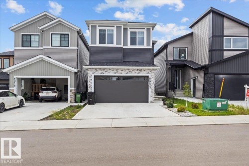 Modern two-story home featuring a striking stone and siding exterior, dark-framed garage door with matching architectural detailing, and a clean concrete driveway - 6903 169 Avenue Nw, Edmonton, AB - Outdoor With Facade
